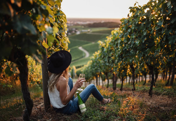 Frau sitzt auf einem Weinberg - mit Federweißer gewappnet