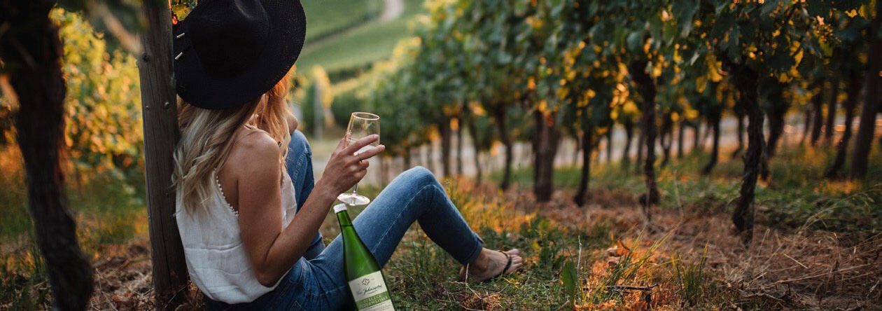 Frau sitzt auf einem Weinberg - mit Federweißer gewappnet